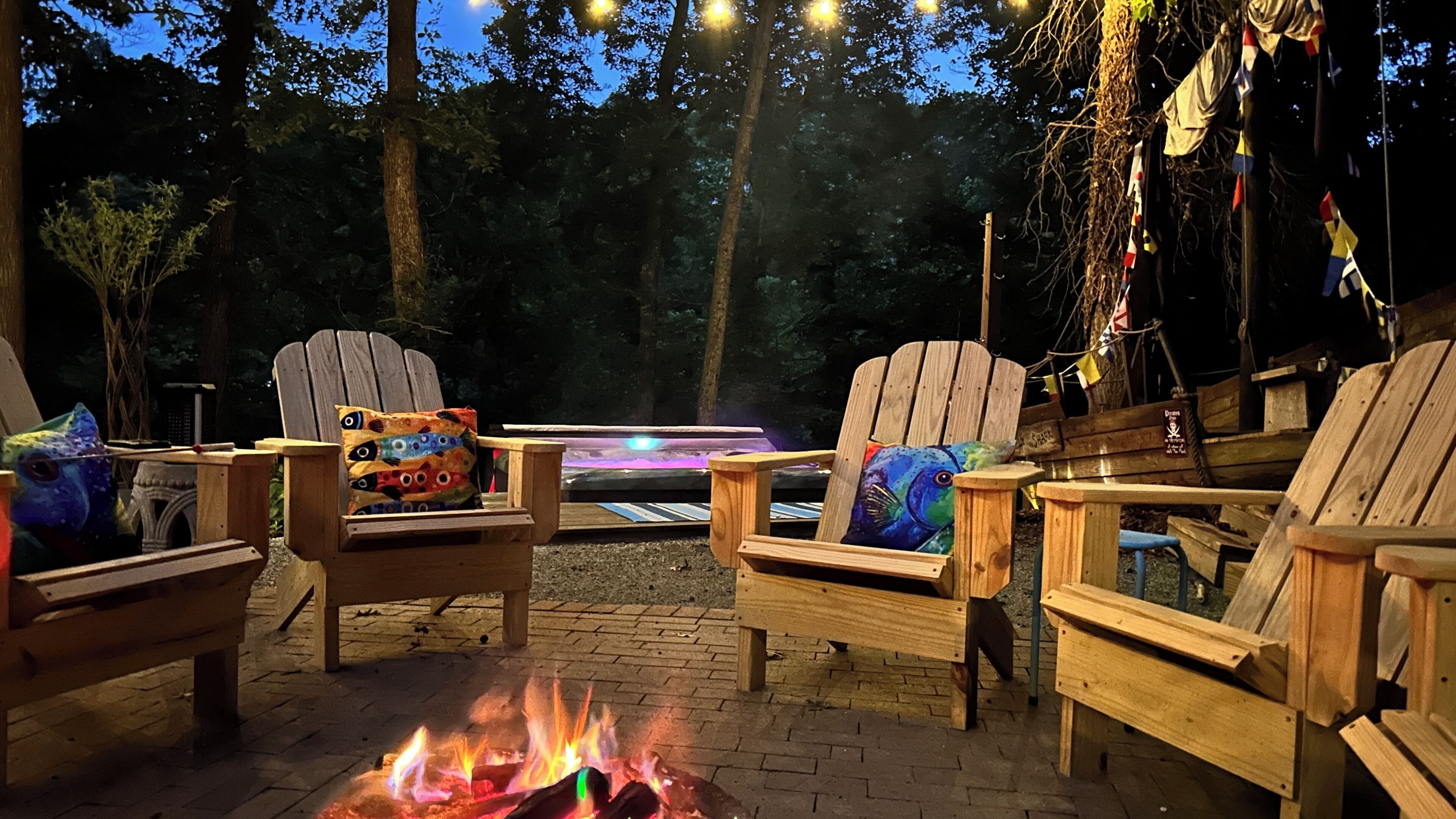 Een terras met houten Adirondack-stoelen, een vuurkorf en lichtjes.