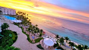A resort with a swimming pool, beach, and palm trees.