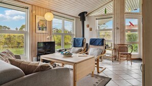 Een gezellige woonkamer met een televisie, houten meubels en grote ramen met uitzicht op het landschap.