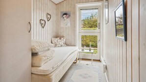 Een knus ingerichte kamer met een bed, een klein tafeltje en een raam met uitzicht op groen.
