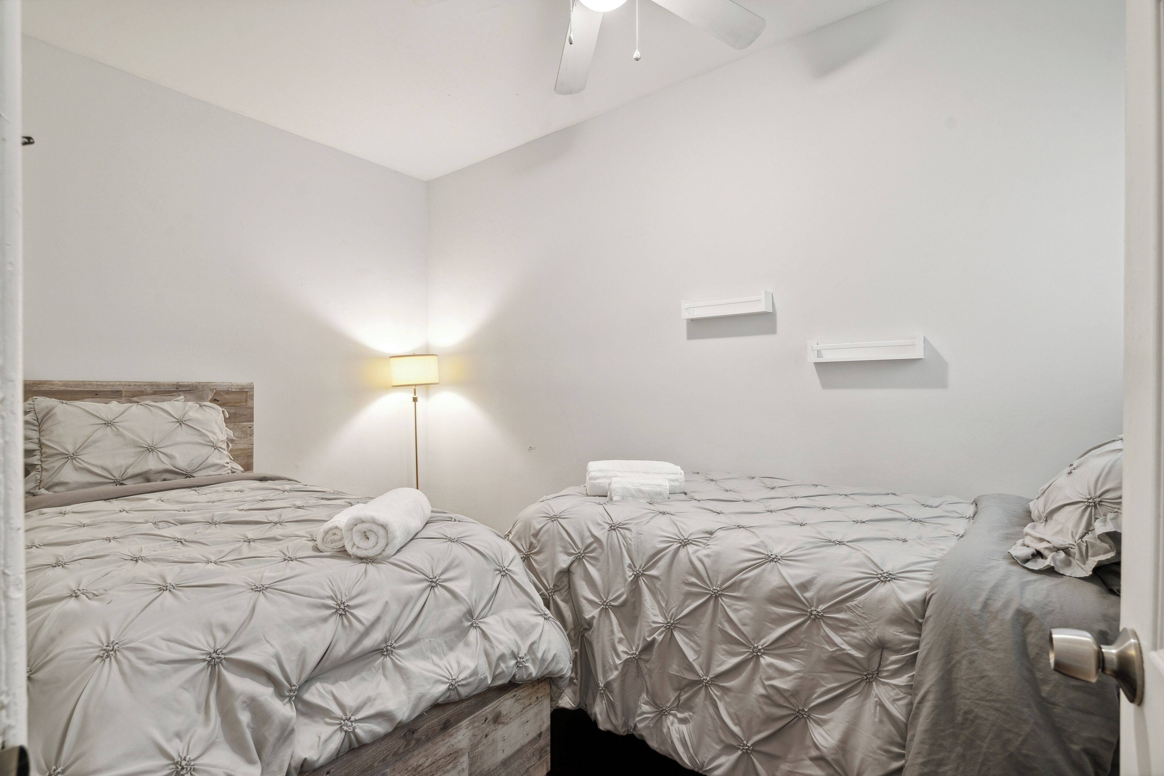 Une chambre avec deux lits, une table de chevet, une lampe et un ventilateur de plafond.