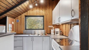 Eine moderne Küche mit Holzwänden, einem großen Fenster, Edelstahlgeräten und einer weißen Arbeitsplatte.