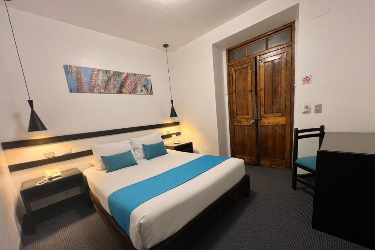 Una habitación de hotel con cama, mesitas de noche, escritorio y armario.