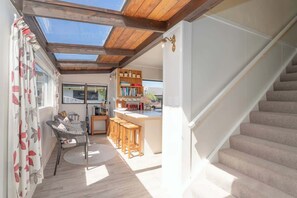 A modern kitchen with a wooden ceiling, a dining area with a round table and chairs, and a staircase.