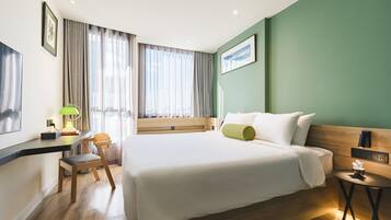 Habitación de hotel con una cama grande, un escritorio, una silla, una mesita de noche y una ventana con cortinas.