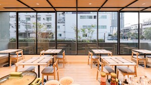 Restaurante com mesas e cadeiras de madeira, amplas janelas com vista para a cidade e design de interiores moderno.
