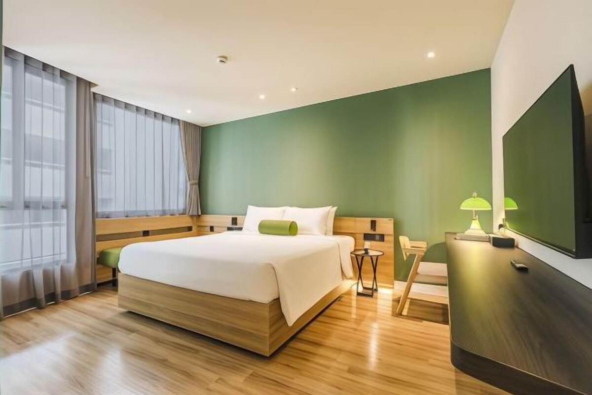 A modern hotel room with a large bed, a wooden headboard, a TV, and a small side table.