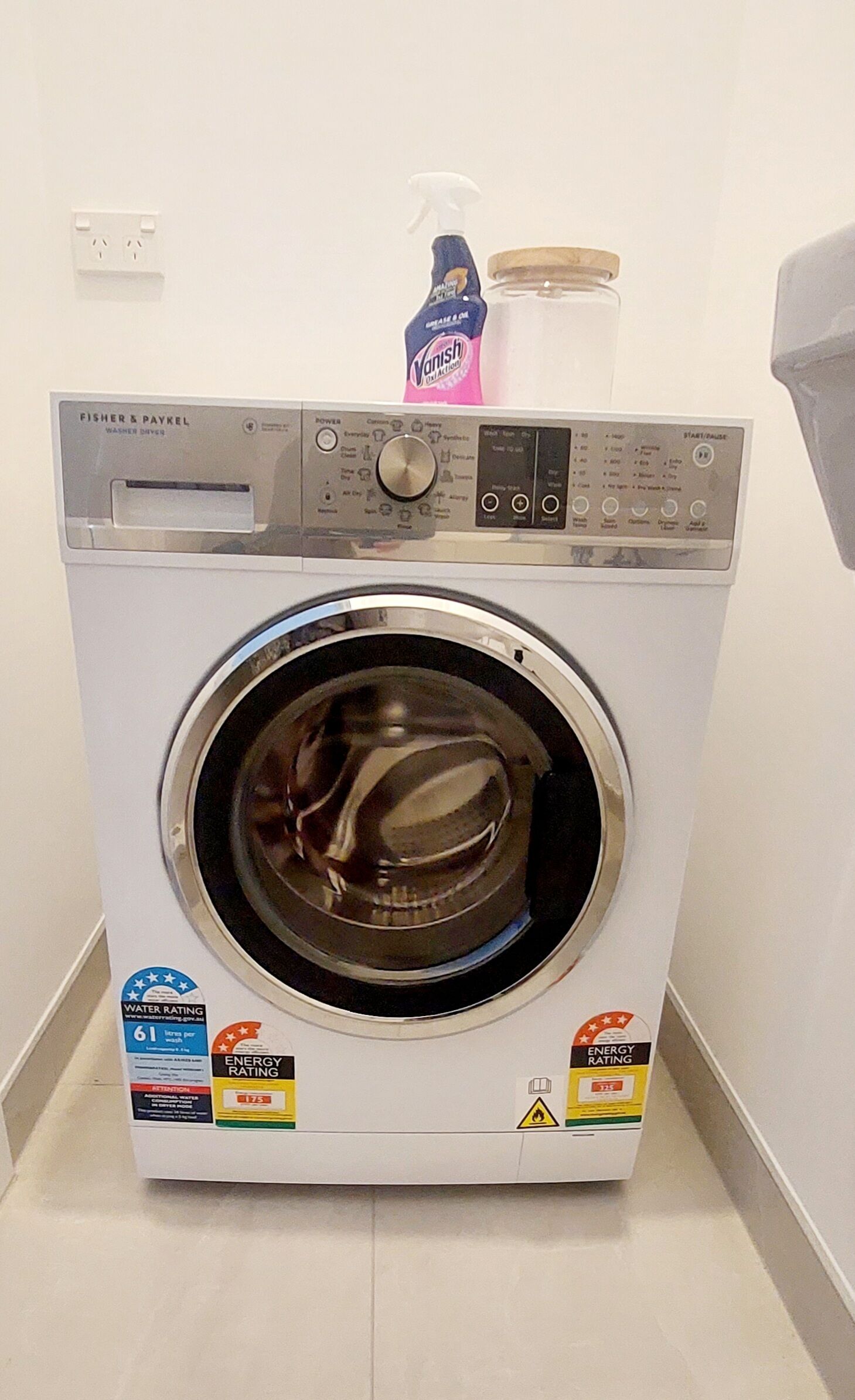 Eine Waschmaschine von Fisher & Paykel mit Kennzeichnung für den Wasserverbrauch, Energieverbrauch und einer Flasche Waschmittel darauf.