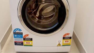 Eine Waschmaschine von Fisher & Paykel mit Kennzeichnung für den Wasserverbrauch, Energieverbrauch und einer Flasche Waschmittel darauf.