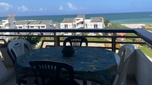 Ein Balkon mit Tisch und Stühlen mit Blick auf Strand und Gebäude.