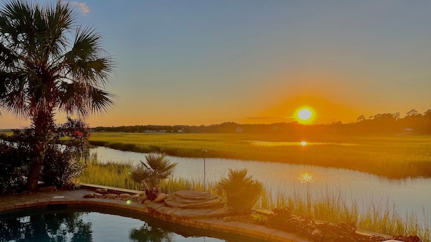 A swimming pool with a view of a sunset over a rice field. - Cottage Time - Marsh Front in Garden City Beach, SC (Garden City)