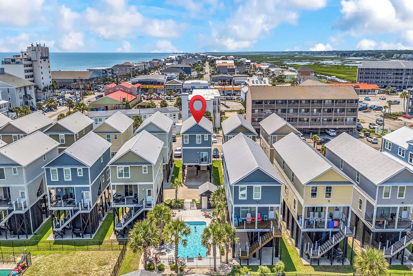 A coastal hotel with multiple-story buildings, a central pool, and a view of the ocean.
