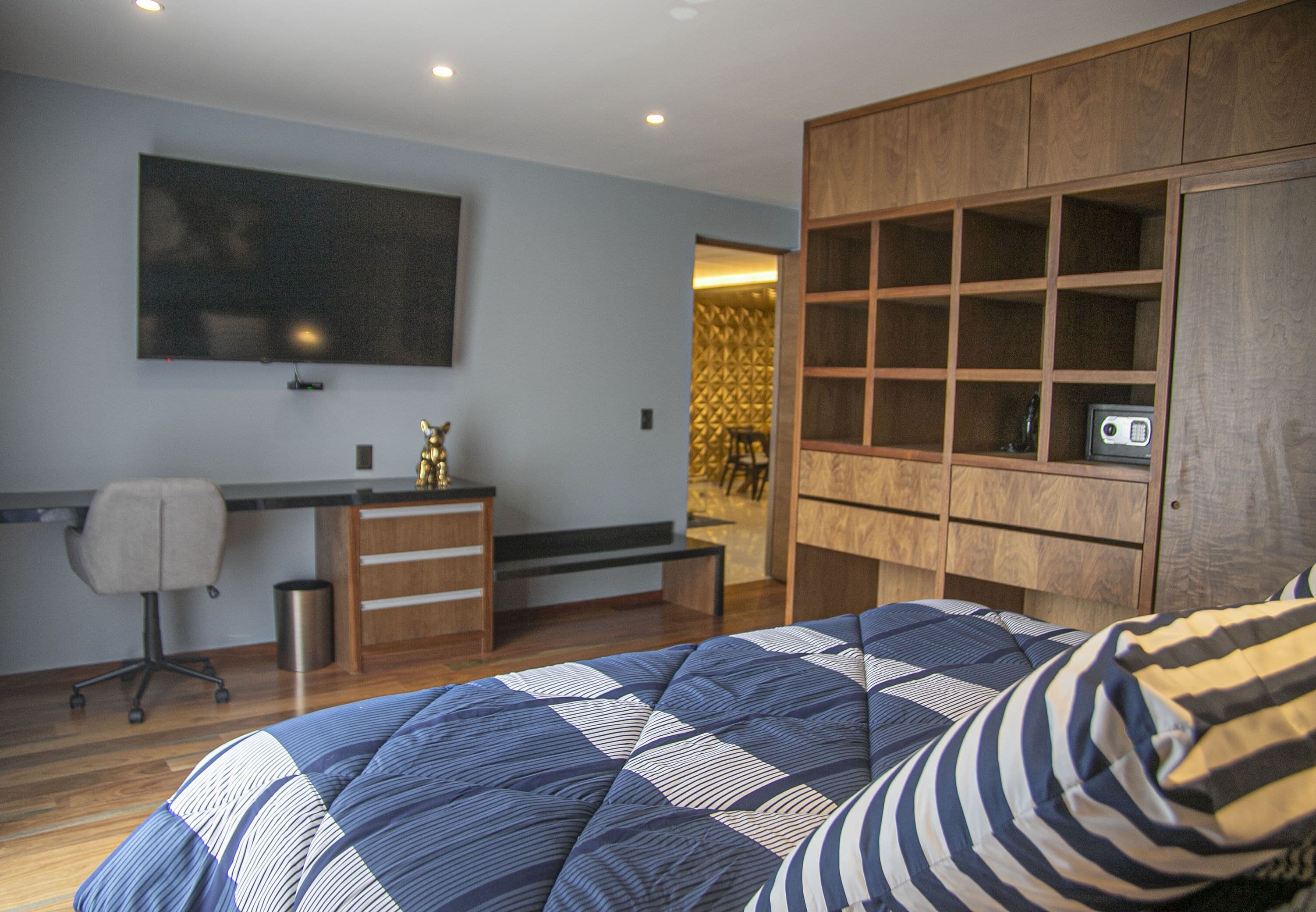 Quarto com cama, escrivaninha, cadeira, televisão e guarda-roupa.