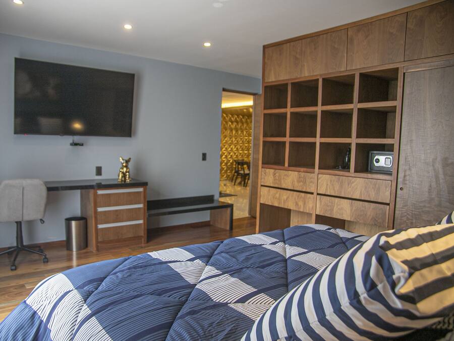 Quarto com cama, escrivaninha, cadeira, televisão e guarda-roupa.