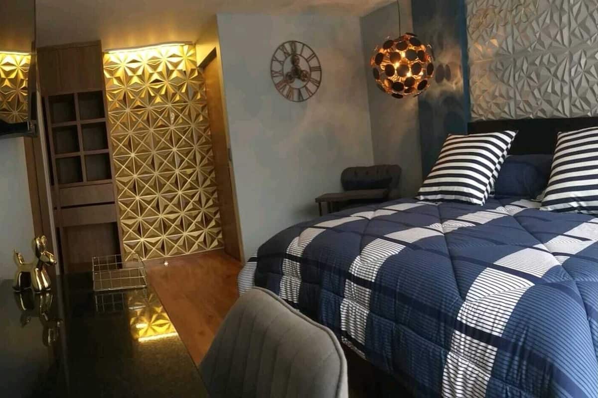 A modern bedroom with a geometric-patterned wall, a bed with striped bedding, a round wall clock, and a unique spherical light fixture.