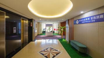 A hotel lobby with a central reception desk, a green carpeted area, and a large illuminated ceiling.