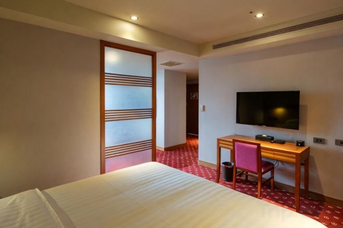 A hotel room with a bed, a desk, a chair, a television, and a sliding door.
