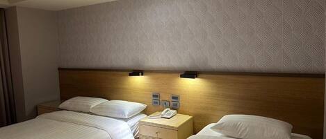A hotel room with two beds, a wooden headboard, a patterned wall, and a nightstand with a phone.