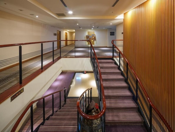 A hotel corridor with a central staircase, wooden paneling on the right, and a sign indicating the direction to the lobby. - Rich & Free Hotel - Fuzhong (New Taipei City)