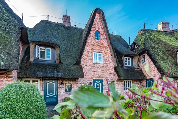 Ein traditionelles Backsteinhaus mit steilem Dach, mehreren Schornsteinen und einem kleinen Fenster mit blauem Rahmen.