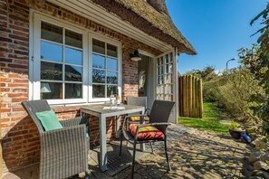 Ein Backsteinhaus mit Strohdach, eine Terrasse mit Tisch und Stühlen sowie ein Garten mit Holzzaun.