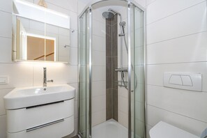 Ein modernes Badezimmer mit einer gläsernen Dusche, einem weißen Waschbecken und einem Spiegel darüber.