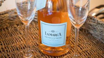 Una bottiglia di Prosecco Rosé con due bicchieri da vino vuoti su un sottopiatti intrecciato.