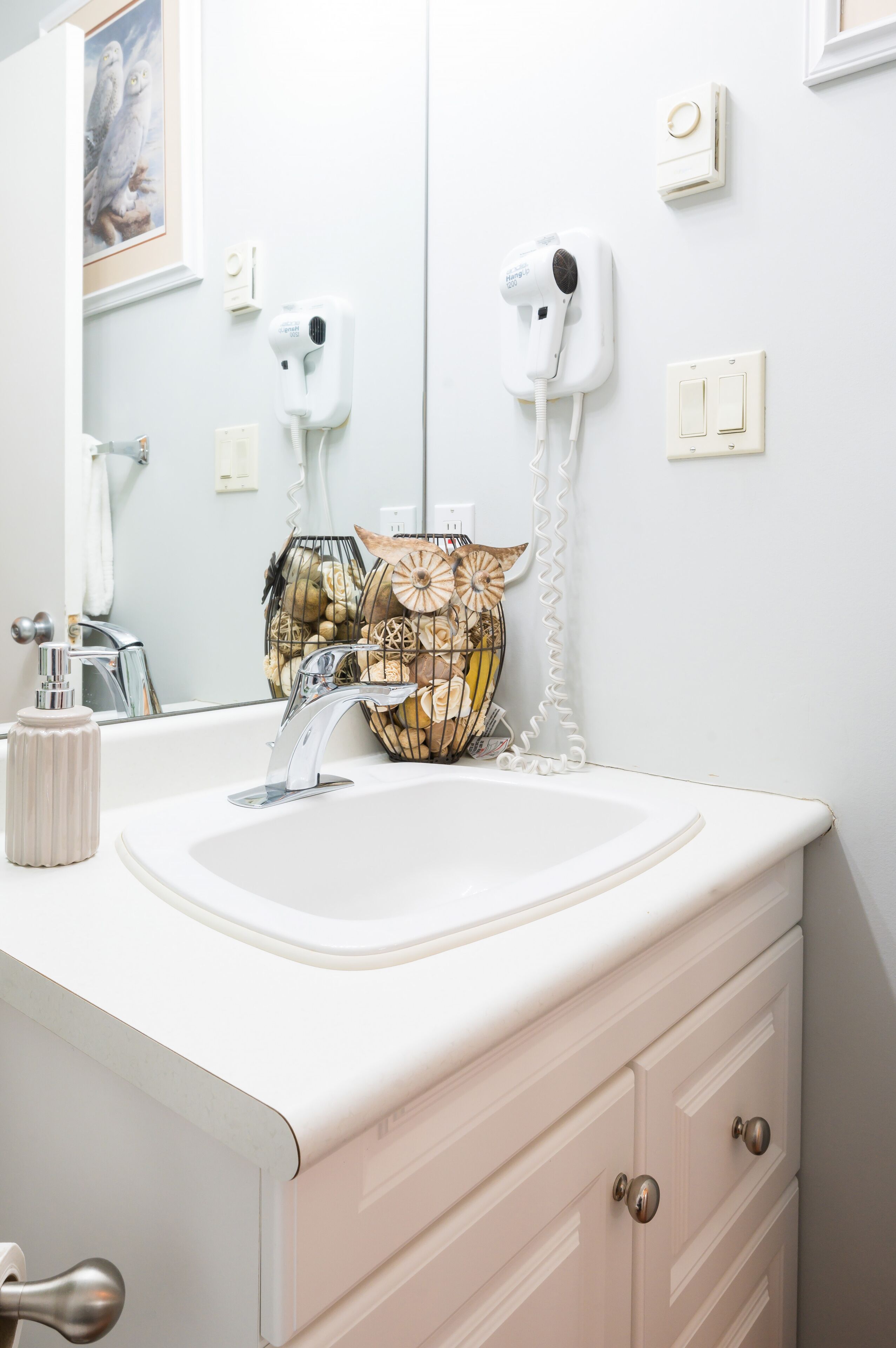 Un baño con lavamanos blanco, un espejo, un secador de pelo y un florero decorativo.