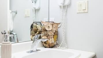 Un baño con lavamanos blanco, un espejo, un secador de pelo y un florero decorativo.