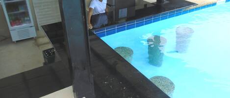 Een zwembad met helderblauw water, omringd door een zwart terras. Er liggen rotsen in het zwembad en iemand is zichtbaar in de buurt van de rand.