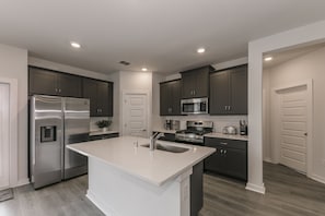 Una cocina moderna con una isla central, electrodomésticos de acero inoxidable, armarios oscuros e iluminación empotrada.