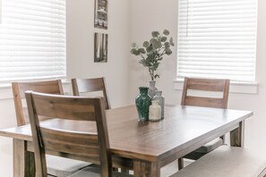 Una mesa de comedor con cuatro sillas de madera, un florero con follaje verde y dos botellas pequeñas sobre la mesa.