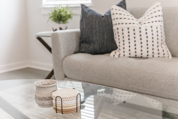 Una sala de estar moderna con una mesa de centro de vidrio, un sofá color beige y almohadones decorativos.