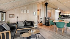 Een modern interieur met een houten plafond, een zwarte leren bank, een eethoek met groene stoelen en een zichtbare keuken.
