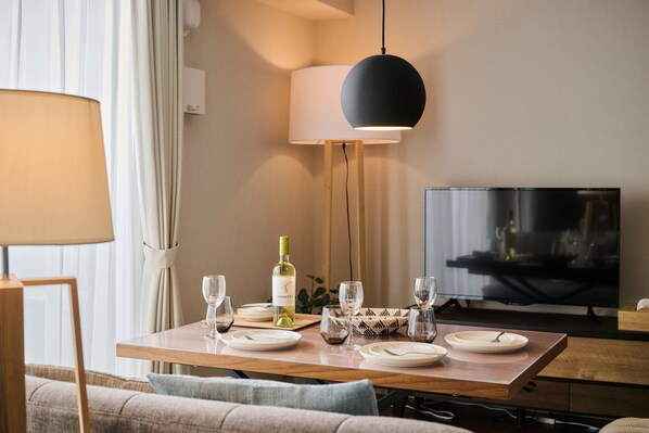 Une table à manger dressée avec des assiettes, des verres et une bouteille de vin, avec un téléviseur et des rideaux en arrière-plan.