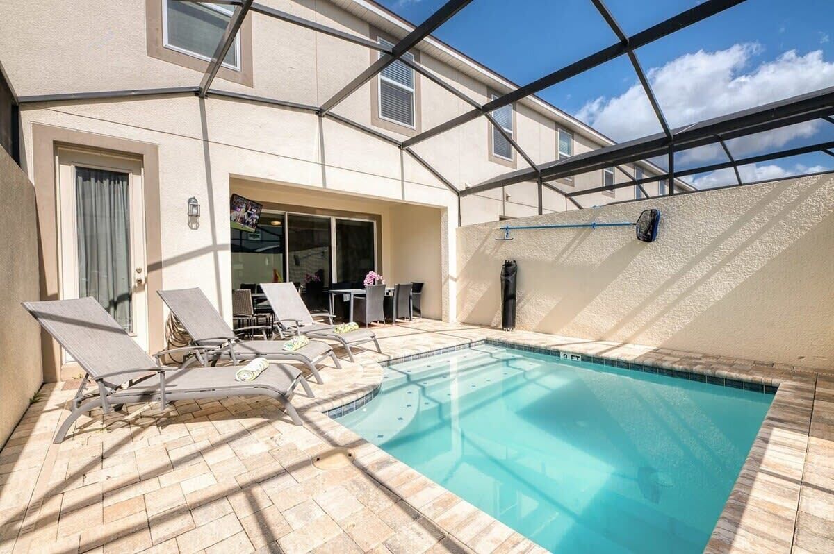 Ein Schwimmbad mit Liegestühlen, einer überdachten Terrasse und Blick zum Himmel.