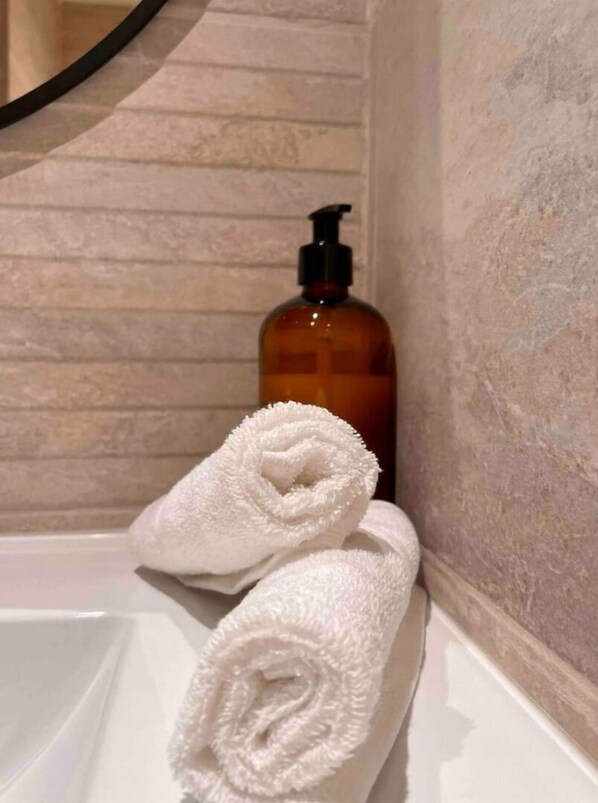 Une salle de bain avec une baignoire, une serviette blanche et un flacon de savon liquide.