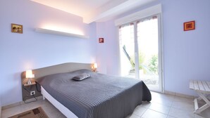 Een slaapkamer met een bed, nachtlampjes, een raam en een klein tafeltje.