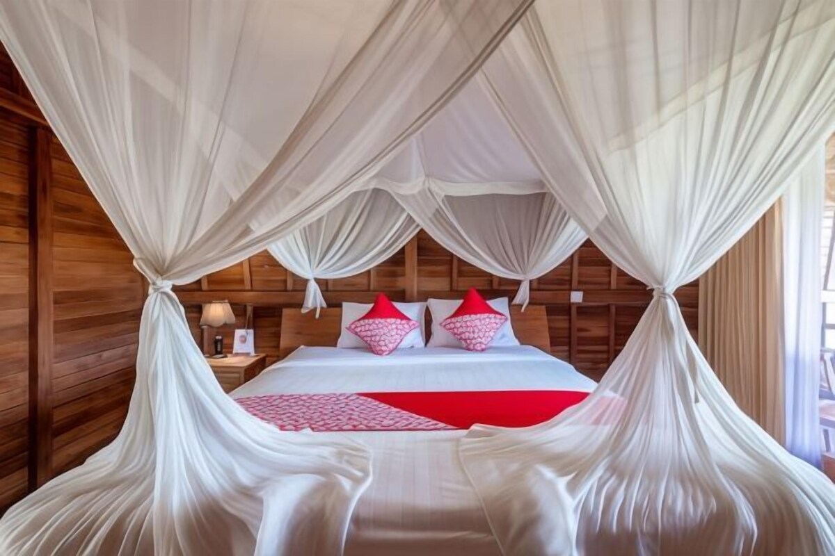 A room with a bed under a canopy, wooden walls, and a nightstand with a lamp.