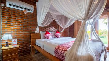 A bedroom with a brick wall, wooden bed frame, white bedding, red and white pillows, and a canopy bed.