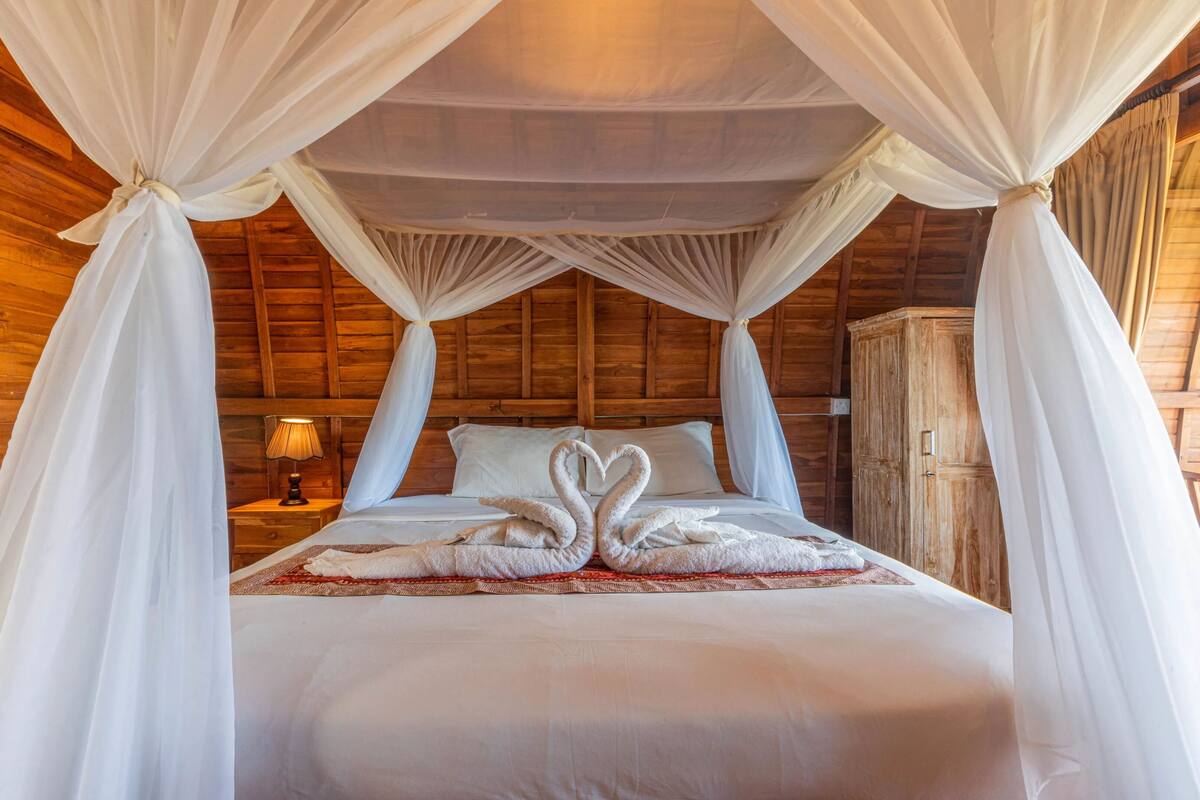 A bed with a canopy, a nightstand with a lamp, and a wooden wardrobe.