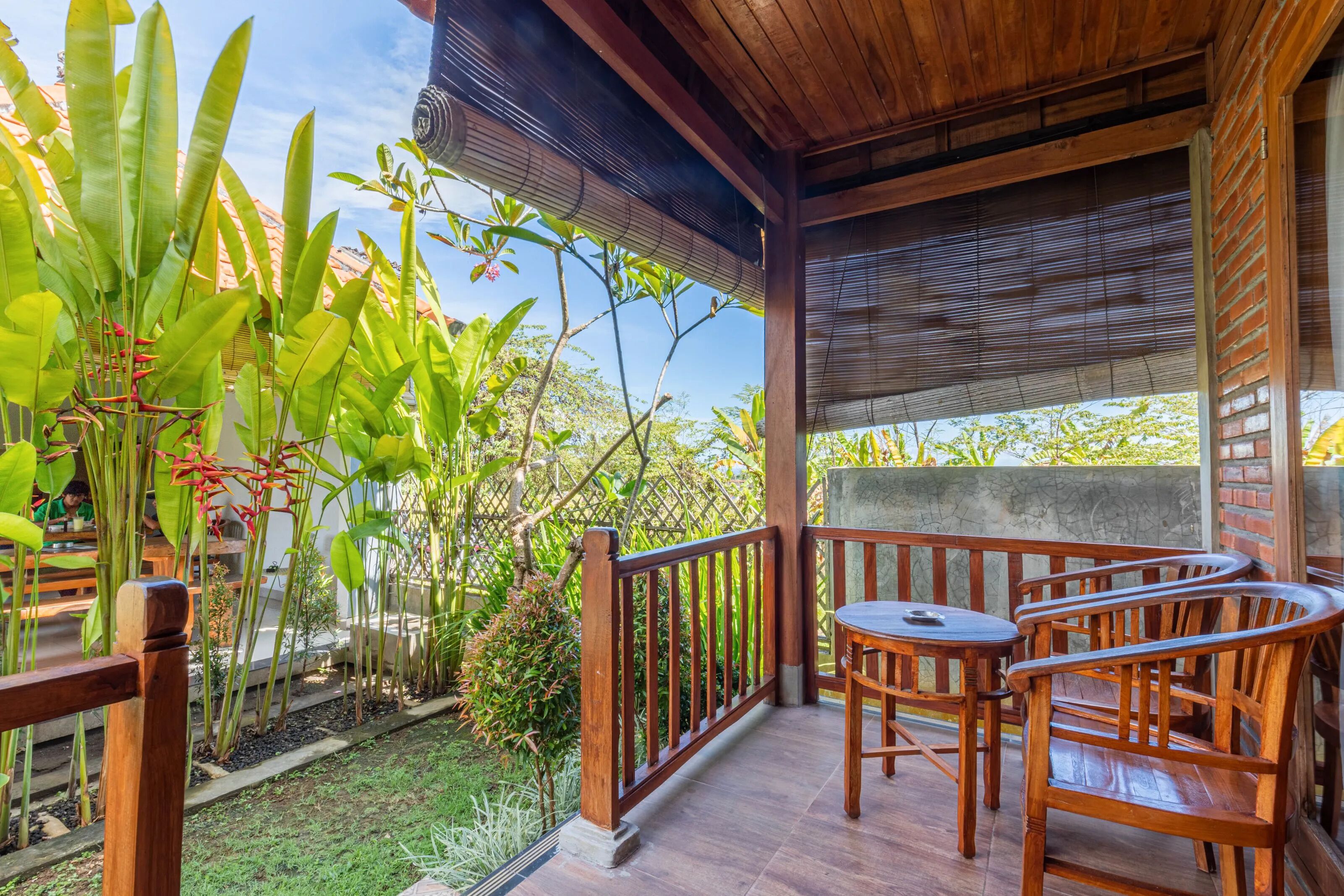 A wooden deck with a table and chairs, surrounded by lush greenery and a view of the sky.