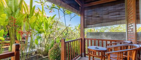 A wooden deck with a table and chairs, surrounded by lush greenery and a view of the sky.