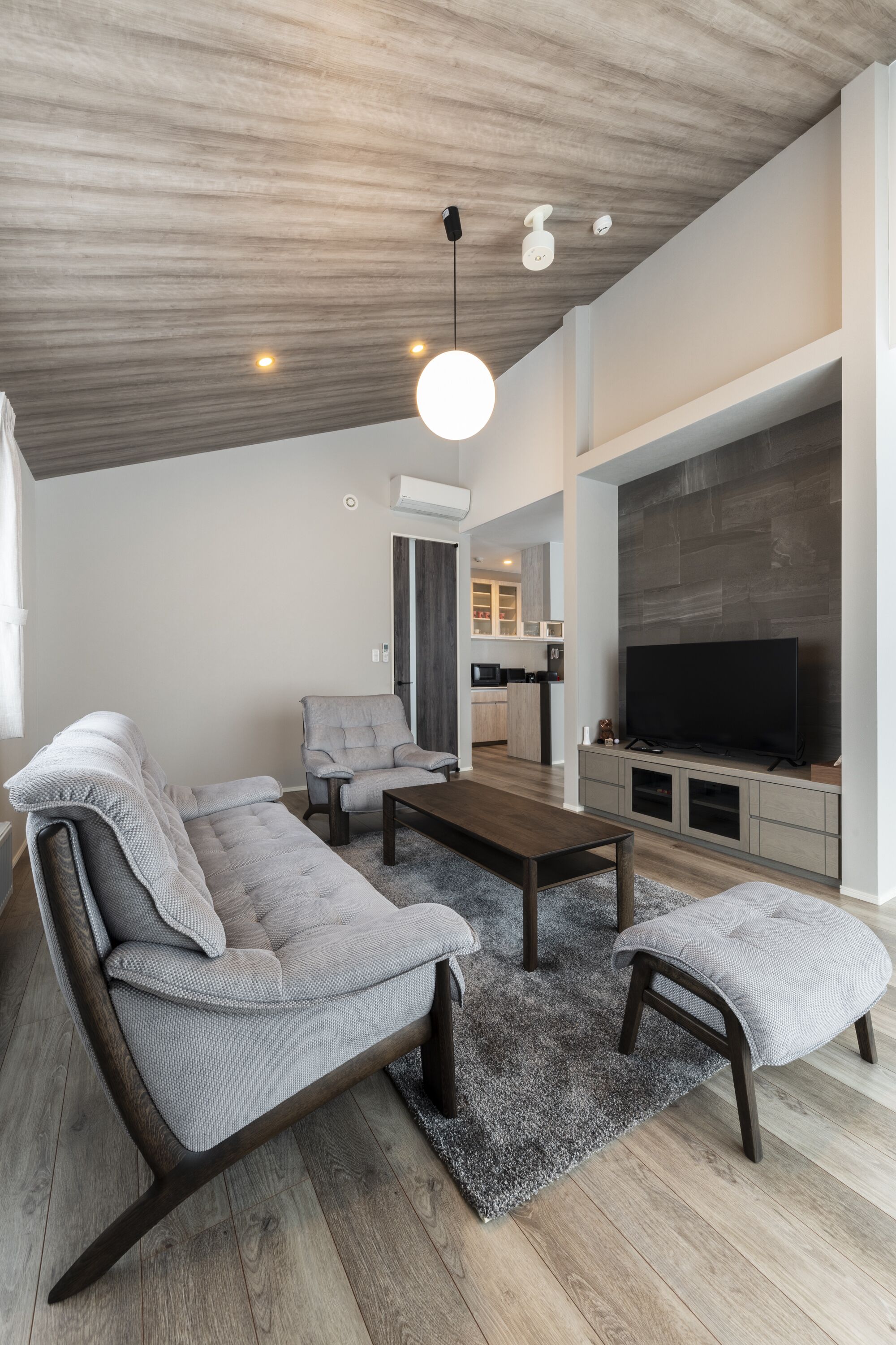 Un salon moderne avec un canapé d’angle, une table basse et un téléviseur fixé au mur.