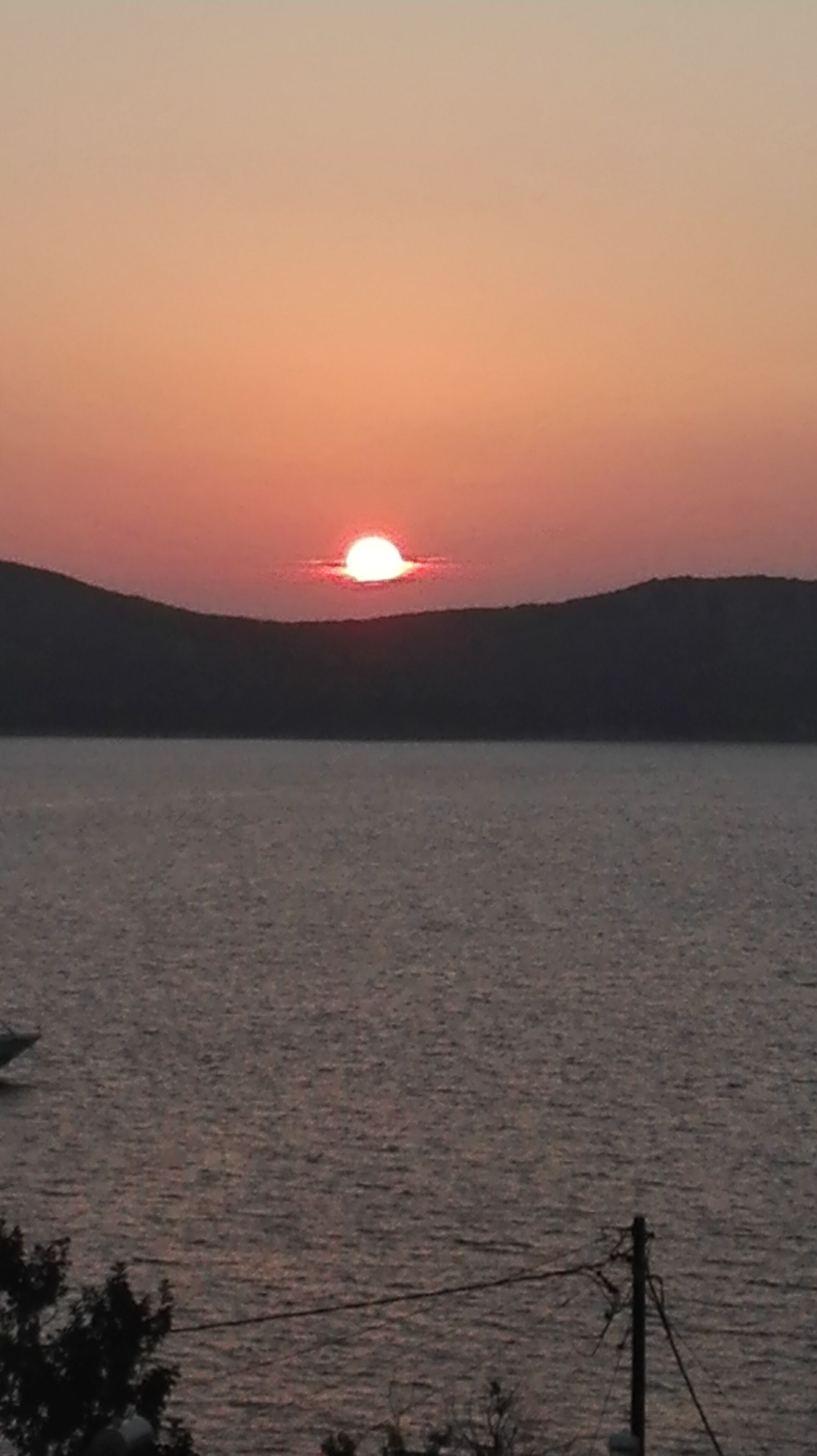 Solnedgang over vand med bakker i baggrunden.