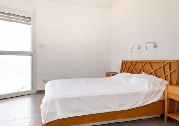 A bedroom with a wooden bed, a nightstand, and a wall-mounted lamp. - Amazing Sea View 3 BR APT Iconic Tower (Bat Yam)