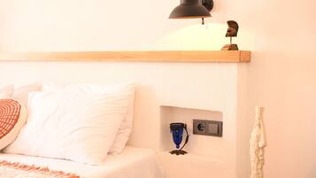 Un dormitorio ordenado con cama, mesita de noche, lámpara y un pequeño estante con adornos.