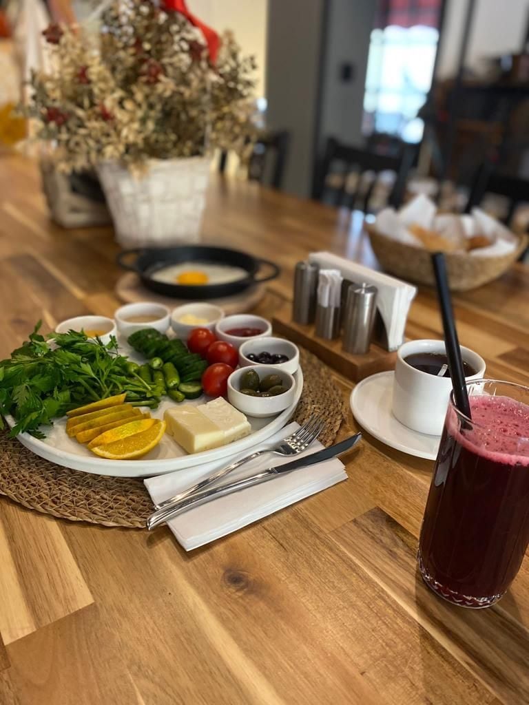 A wooden table with a plate of food, including cheese, vegetables, and olives, and a glass of red drink.
