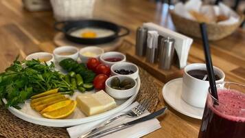 A wooden table with a plate of food, including cheese, vegetables, and olives, and a glass of red drink.