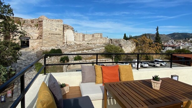 En terrasse med udsigt til gamle ruiner, udendørs møbler og en klar blå himmel.